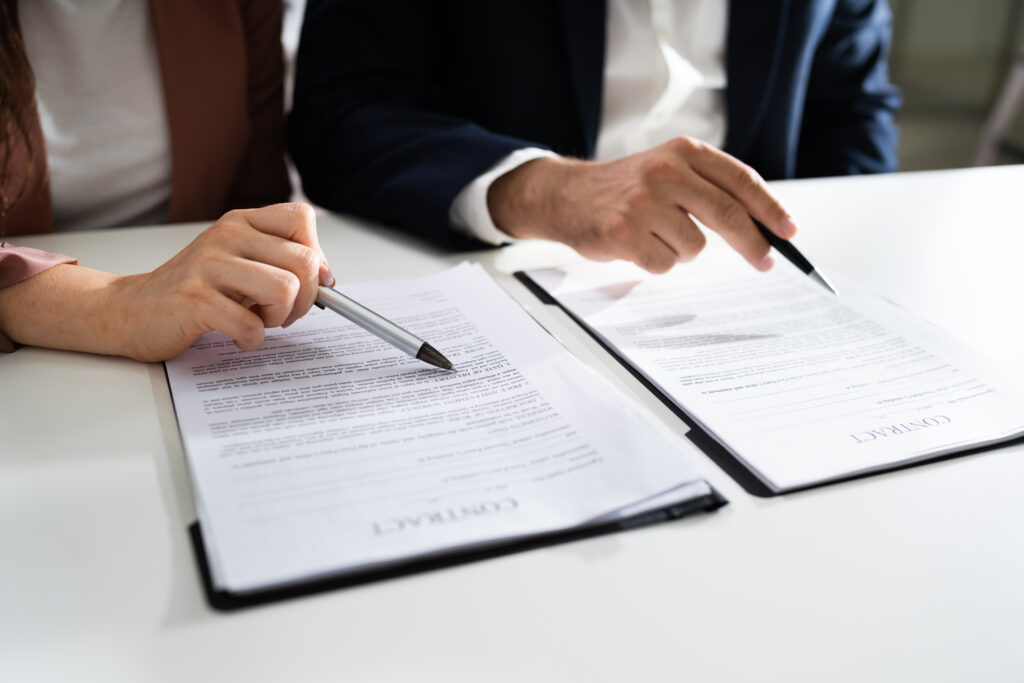 Two people in business attire review and point to details on contract documents laid out on a white desk, each holding a pen—as they discuss the potential for risky use of AI in family law.