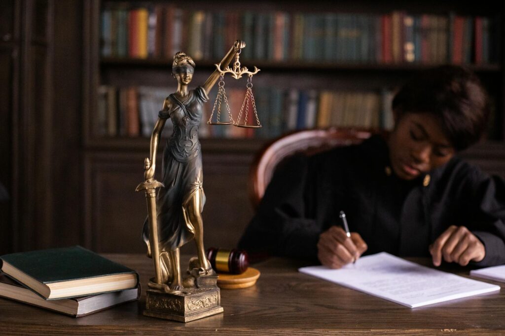 A Guide To Updating Wills, Trusts, And Beneficiary Designations After Divorce In California 1 A judge writes at a desk with a Lady Justice statue, a gavel, and books on trusts and wills in the foreground; bookshelves are in the background.