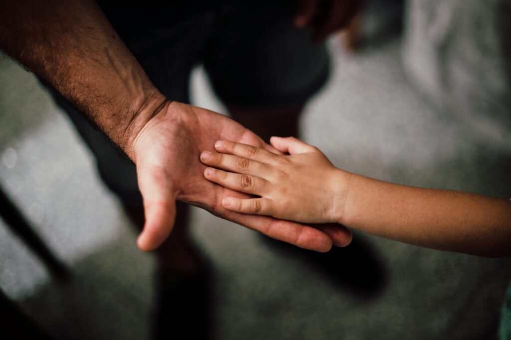 Child Support Modifications In California: When To File & Requirements 1 A child's hand resting on top of an adult's open palm, both hands facing upward on a neutral background—symbolizing support and guidance through California child support modifications and requirements.
