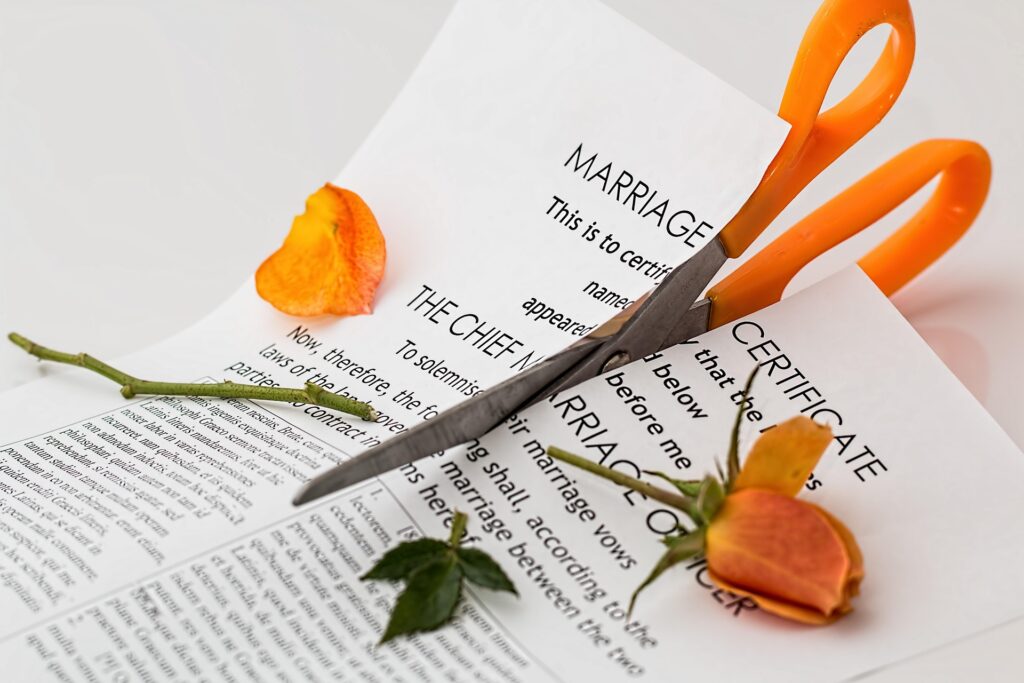 Key Factors That Impact the Timeline of a High Asset Divorce in California 1 A pair of orange-handled scissors cutting through a marriage certificate with a wilted yellow rose and rose petals nearby, symbolizing a high asset divorce in California.