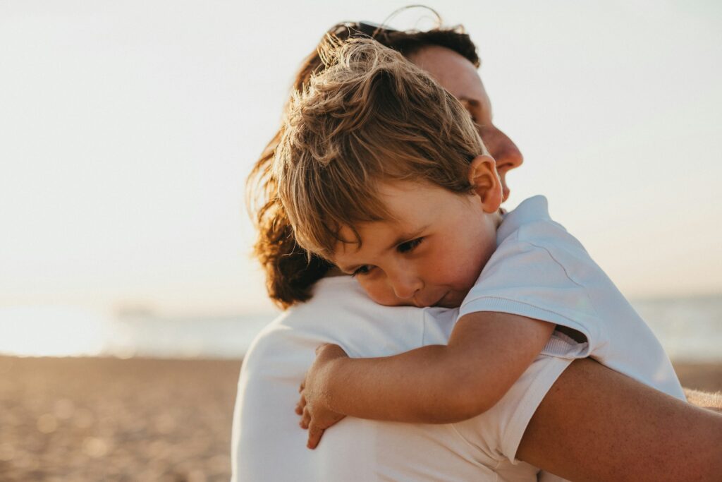 4 Things Parents Wish They Understood About Custody Before Divorce in California 2 An adult holds a young child in their arms on a beach, with the child resting their head on the parent's shoulder—a tender moment that can be especially meaningful for parents navigating custody after divorce in California. The scene is softly lit by natural sunlight.