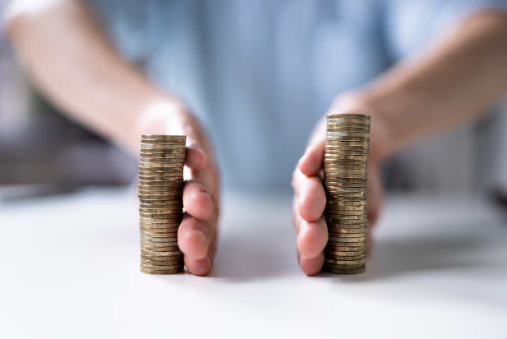 A person separates two stacks of coins with both hands on a white surface, dividing the coins evenly—much like how finances are distributed during a California divorce when a spouse controls the assets.