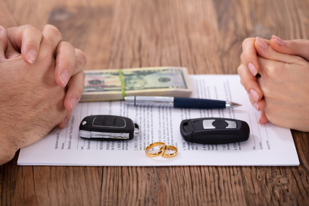 Close-up Of Hands On Divorce Document With Wedding Rings And Car Keys Over Wooden Table