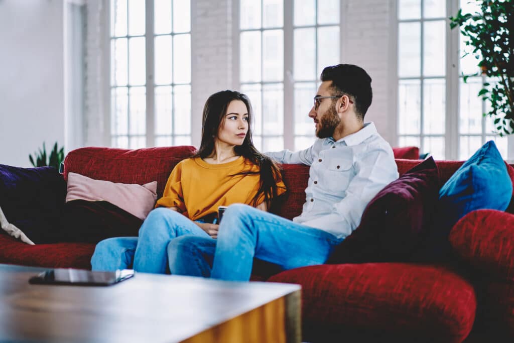 Boyfriend talking with girlfriend discussing plans on weekend resting on comfortable sofa in own apartment, serious couple in love spending leisure time together talking on couch in stylish room